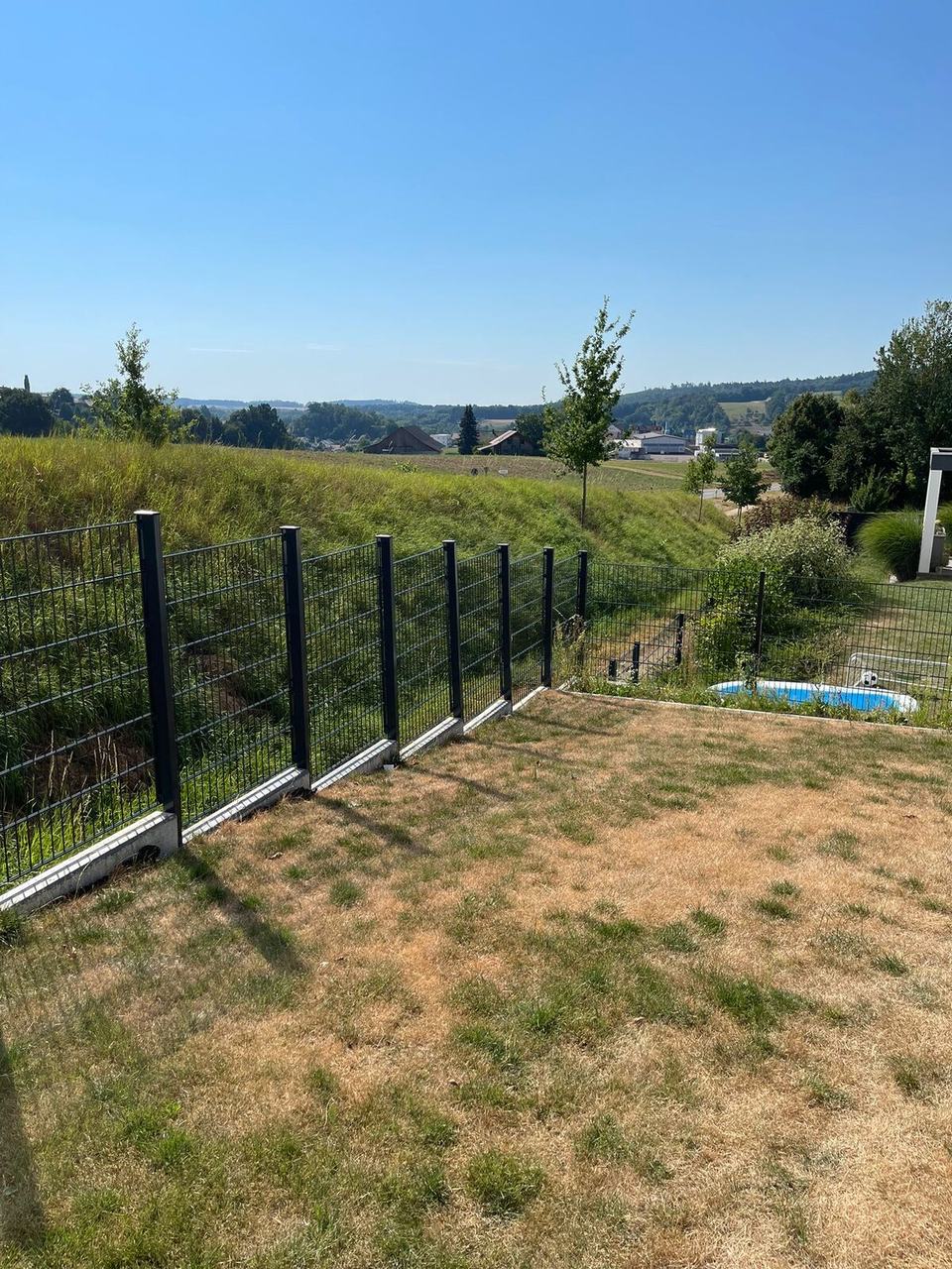 Zaunpfosten und Doppelstabmatten auf Wiese und Hanggrundstück